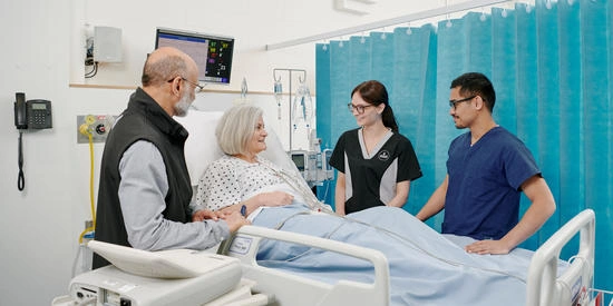 Nursing students in a hospital room talking with a patient in a hospital bed