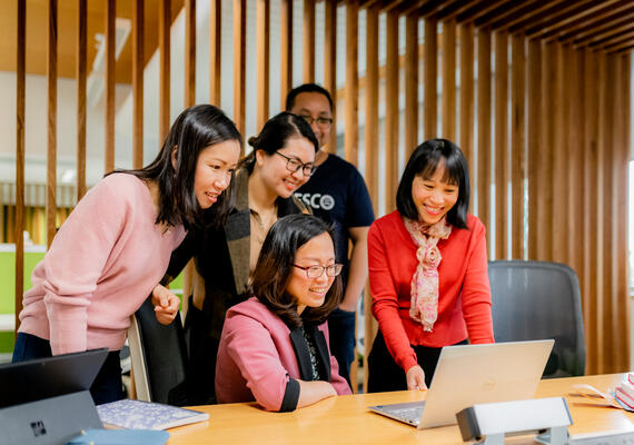 A group of research students lean over to watch a presentation on a laptop 