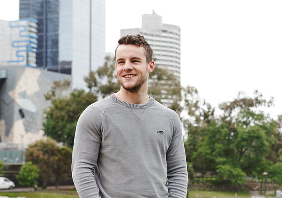 Andrew Keeghan, a student in Deakin's Indonesian degree, is standing in a park.