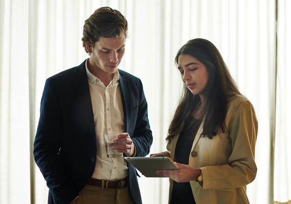 Two students talk while looking at an ipad.