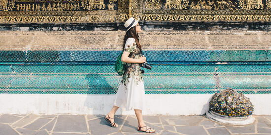 A student with a camera walking outside past a temple in Luang Prabang.