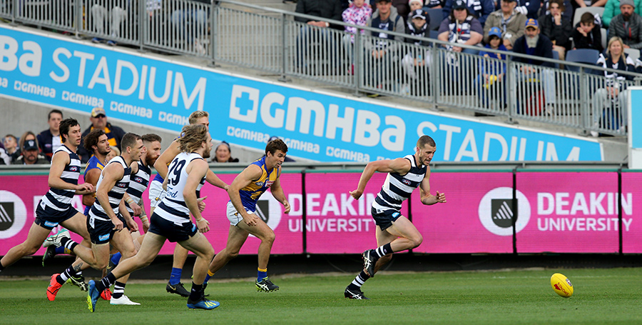 Action shot of AFL Geelong team players playing football on the field together.