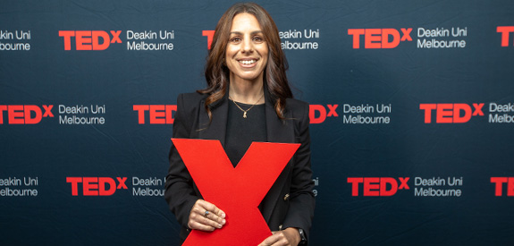 Photo of Dr Dominque Condo holding a red X at Deakin's TEDx event