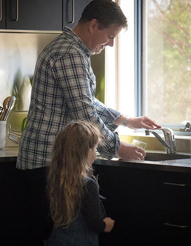 Parent pouring a glass of water with a child using a tap with a water filter.