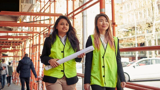 Two Deakin construction students walk on a site wearing high vis vests.