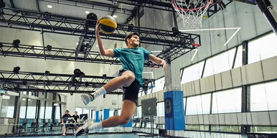 34422_550x275_sport-science-ranking.webp Student about to slam dunk a basketball while two more students watch on from a desk with equipment