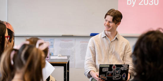 Deakin student teacher sitting and smiling with a laptop in a classroom.
