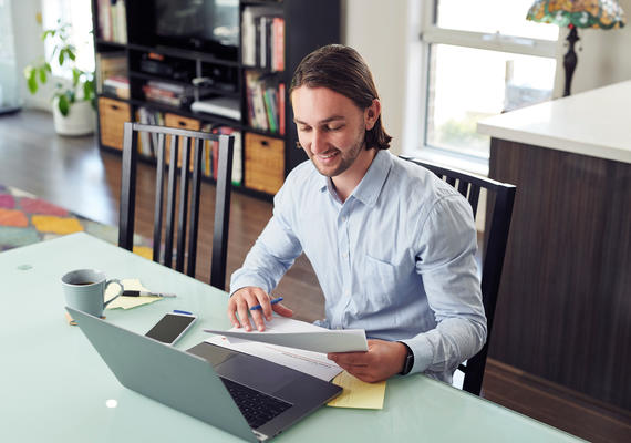 A Deakin student studies online with a laptop. Papers and a phone are on the desk.