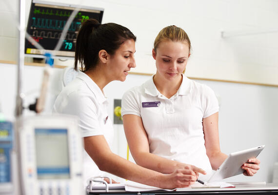 Nursing students in hospital looking at notes with tablet.
