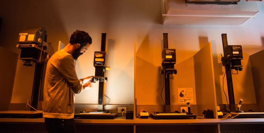 The darkroom and film scanning facility showing four enlargers and with one person standing and using one of these