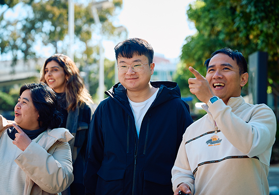 Four students walking outside campus, pointing ahead and smiling.