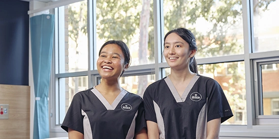 Two Deakin nursing students smiling whilst working on campus.