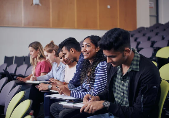 Students sit inside a lecture theatre and take notes.