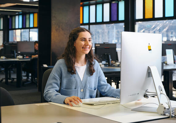 A student in a blue cardigan at a desktop computer.