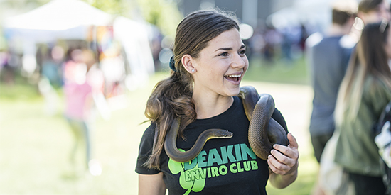 Deakin student smiling and holding a snake on campus.