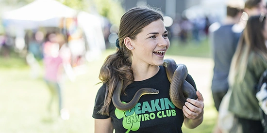 Deakin student smiling and holding a snake on campus.