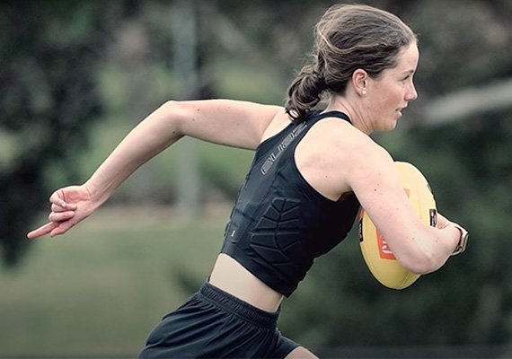 Deakin student runs on a field holding a football.