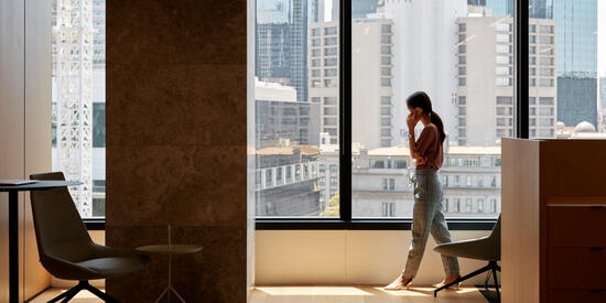 A person in a corporate office talks on the phone in front of a window overlooking the city skyline.