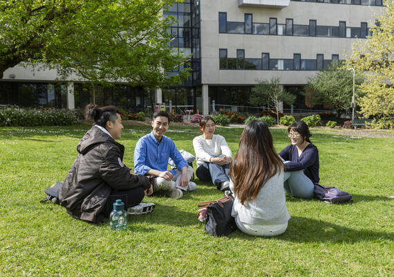 A group of Deakin res students sitting on the grass on campus outside accommodation.