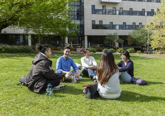 A group of Deakin res students sitting on the grass on campus outside accommodation.