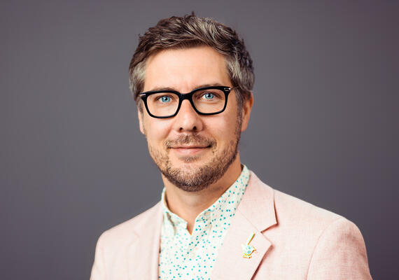 Deakin Doctor Wade Kelly smiling whilst in front of a blank backdrop.