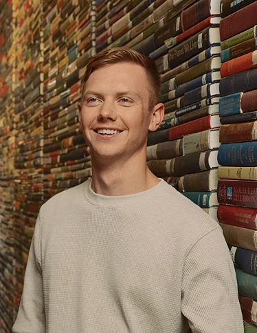 Deakin research student Asher smiling in front of wall of books.