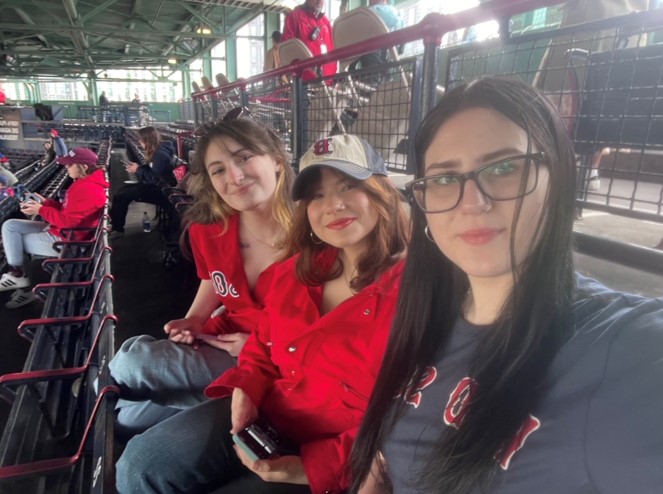 A selfie of Tarnie and two friends sitting in a sports stadium, wearing red merchandise