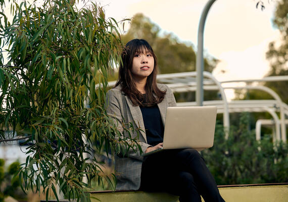 A student uses their laptop while sitting outside in the campus gardens.