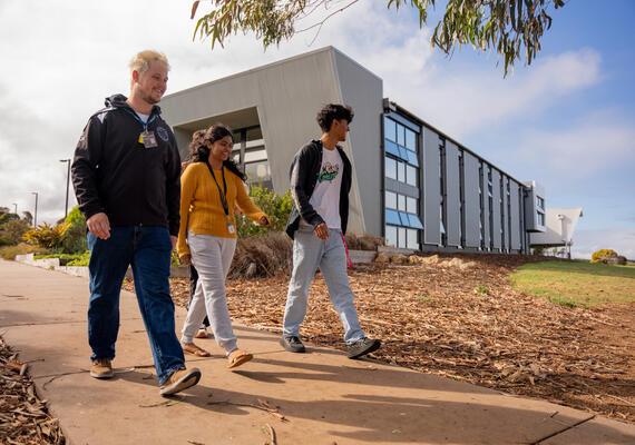 Three Deakin residents outdoors, walking down a pathway with Warrnambool on-campus accommodation behind them.
