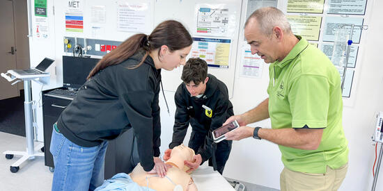 Two students and a teacher practice on a manikin.