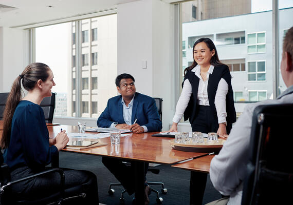 Two male and two female students casually talking to each other around a table in a boardroom.