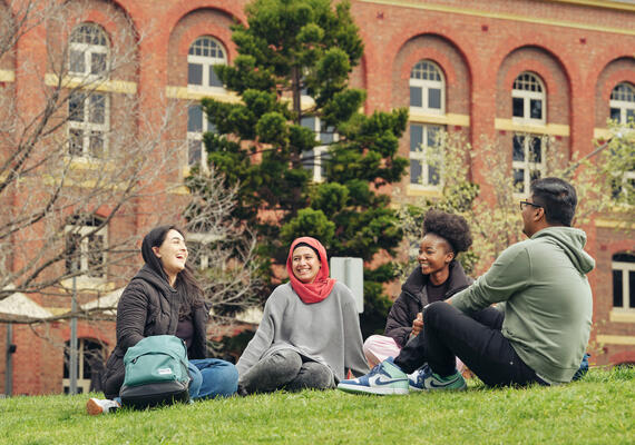Deakin students sitting and talking on grass on campus.