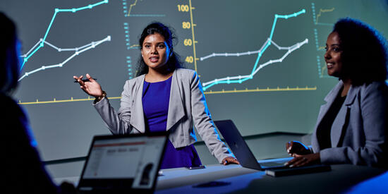 Three students in discussion with digital graphs projected on the wall behind them.