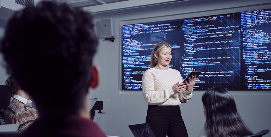 Deakin student standing in front of screens with analytics on campus.