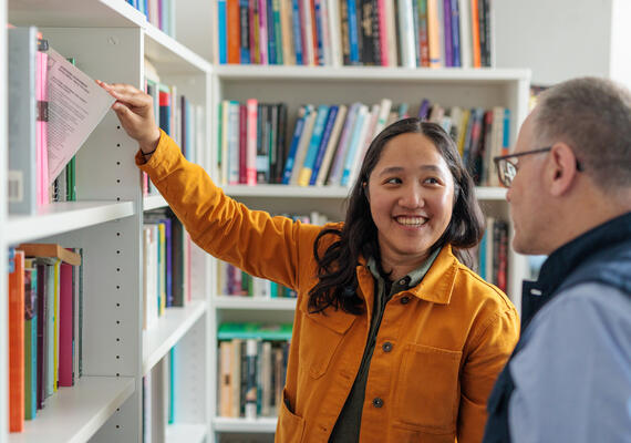 A researcher pull out a book in the library to show supervisor 