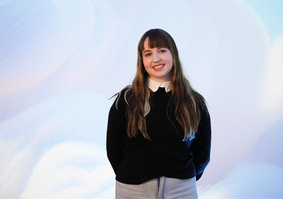 Deakin PhD recipient Kira Hughes standing against a pastel backdrop.