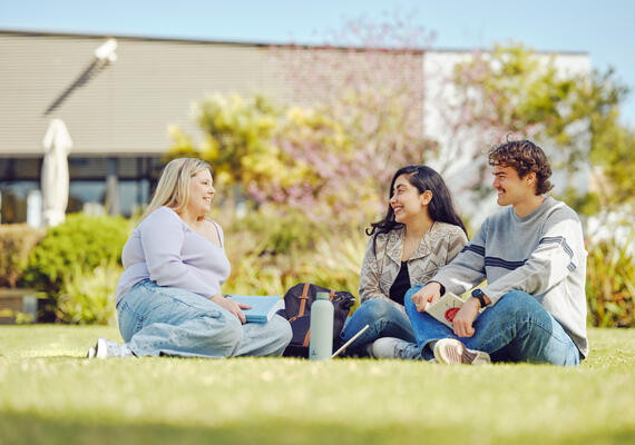 Three students sit on the grass outside on the Geelong Waurn Ponds Campus.