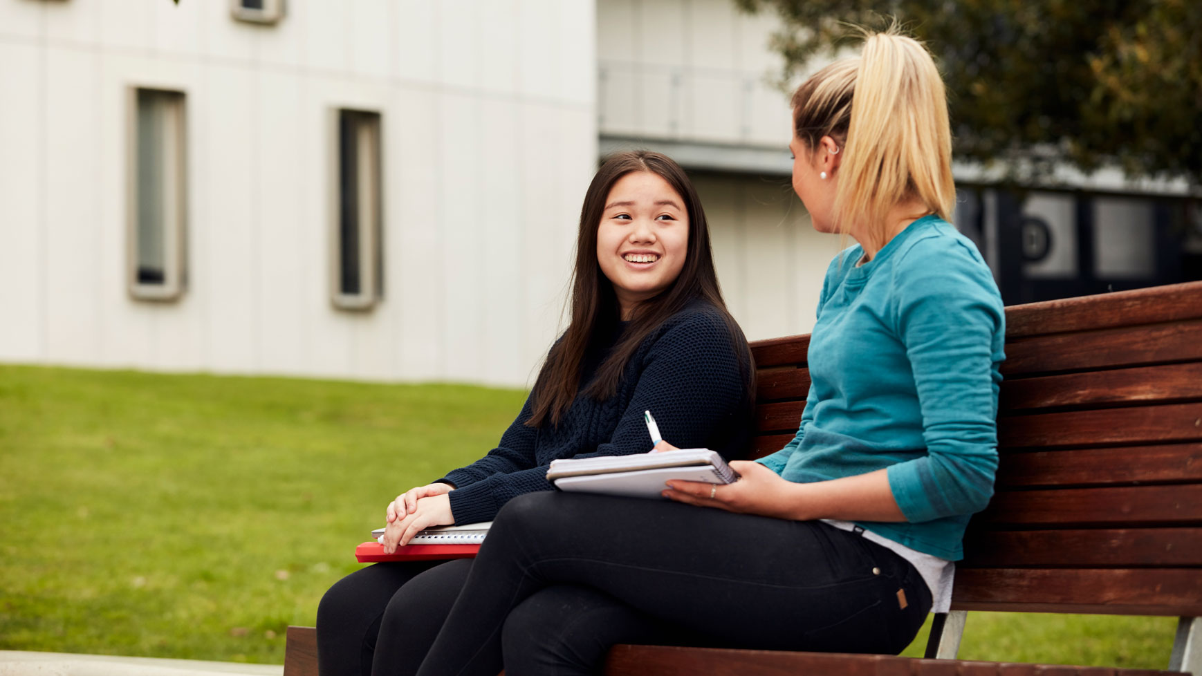A student smiling while talking to a Deakin staff member on a bench outside on campus