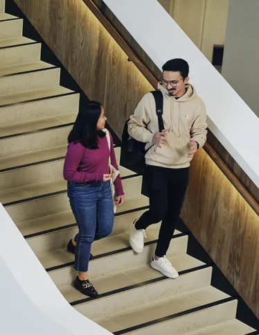 Two Deakin research students smiling and walking on stairs on campus.
