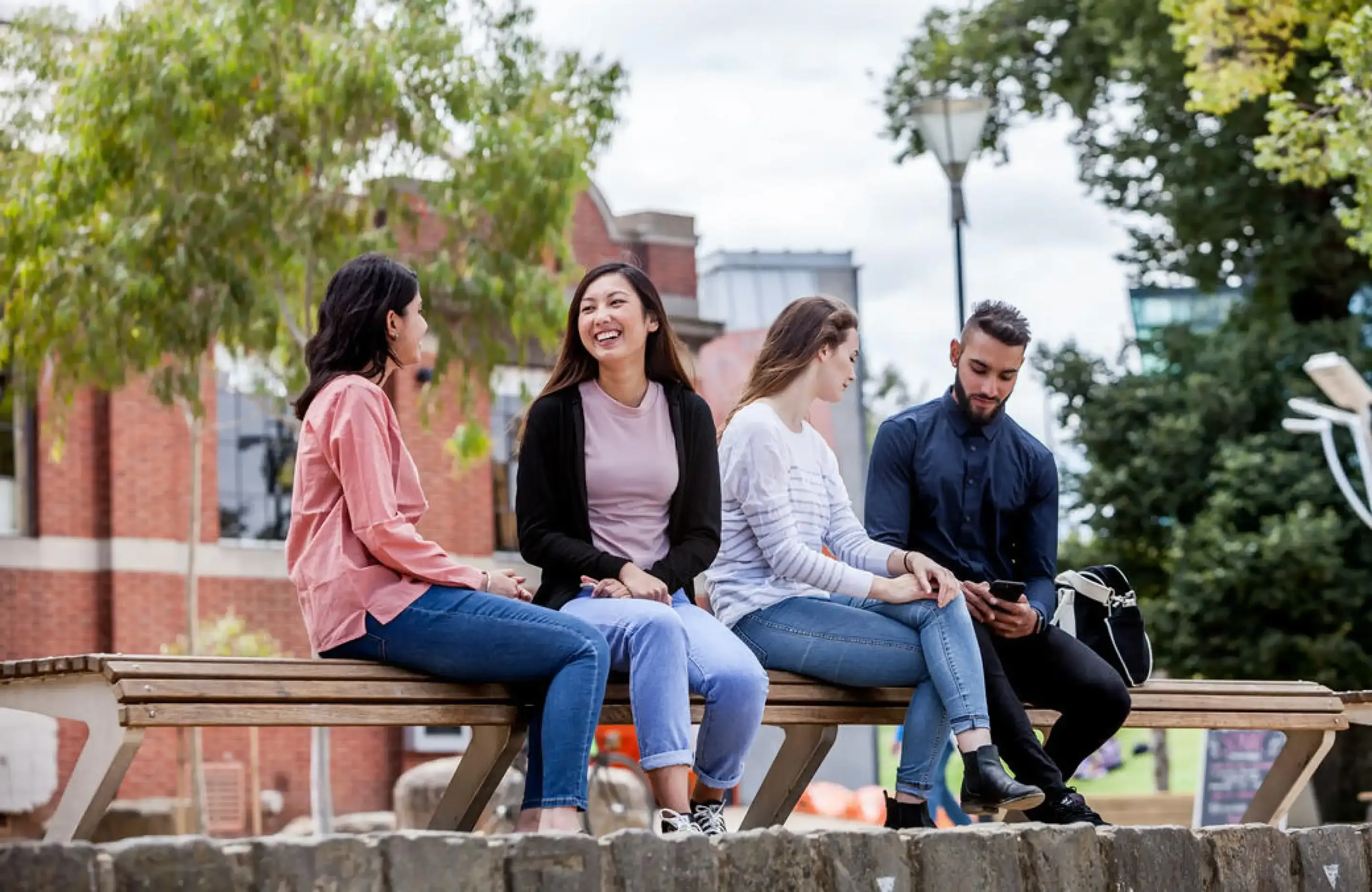 Four students sitting on wall laughing