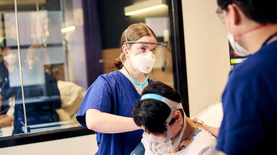 A postgraduate nursing student helping a patient in a hospital bed. 