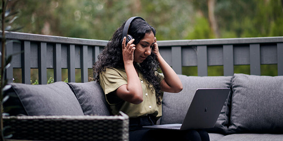 Student sits outside at a table, listening to a Deakin lecture on their laptop.