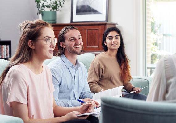 Three Deakin students sit studying on a couch with reading materials.