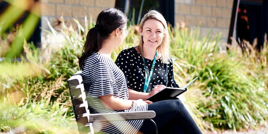 Two health professionals sit outside on a park bench and talk.