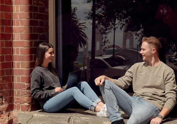 Two people sitting on a brick wall at Deakin's Geelong Waterfront campus