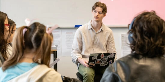 Student teacher sitting with laptop in lap at front of classroom