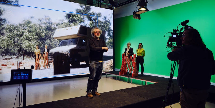 Lecturer addresses students at Deakin's virtual production studio. Standing in front of a green screen with a TV camera recording as they tal