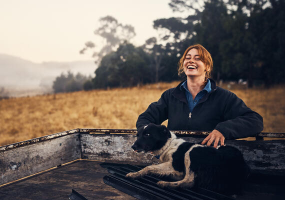 a person smiles standing next to a ute with a dog 
