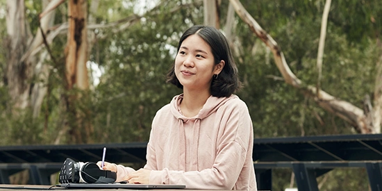 Student smiles while sitting and studying outside at Burwood Campus