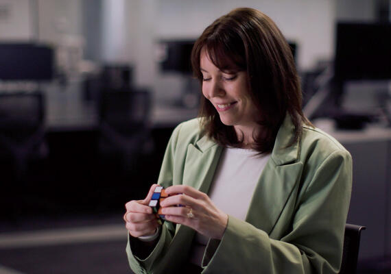 Paige is sitting in a Deakin IT lab, playing with a rubiks cube.